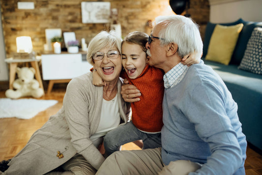 Nonno e nonna che abbracciano e baciano il nipotino seduti per terra in salotto