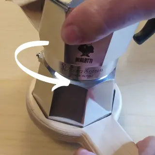 Particolare dell'apertura della moka express tre tazze con l'aprimoka con particolare della direzione di svitamento.