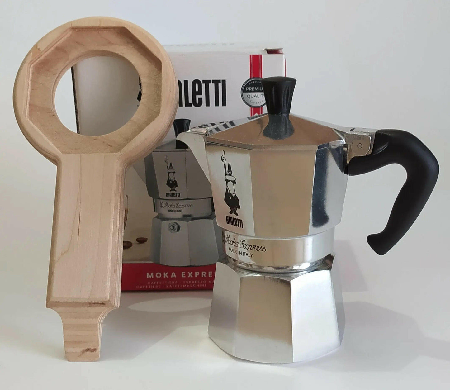 Caffettiera Bialetti Moka express 3 tazze con il suo imballo in cartone sullo sfondo e Aprimoka per Moka Express appoggiato in verticale sull'imballo della caffettiera.