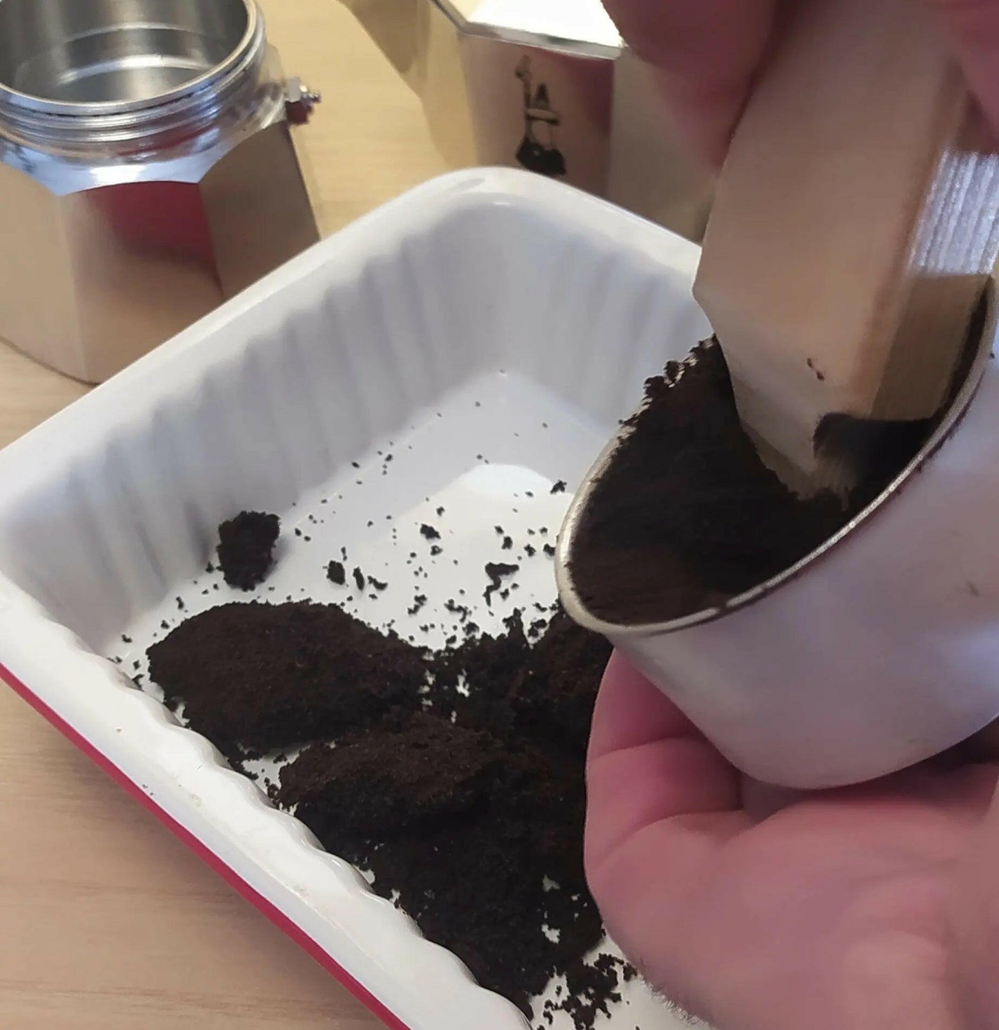 Aprimoka che rimuove ul vecchio caffè dal porta caffè sull sfondo una Caffettiera Bialetti Moka Express 3 tazze svitata usando l'aprimoka
